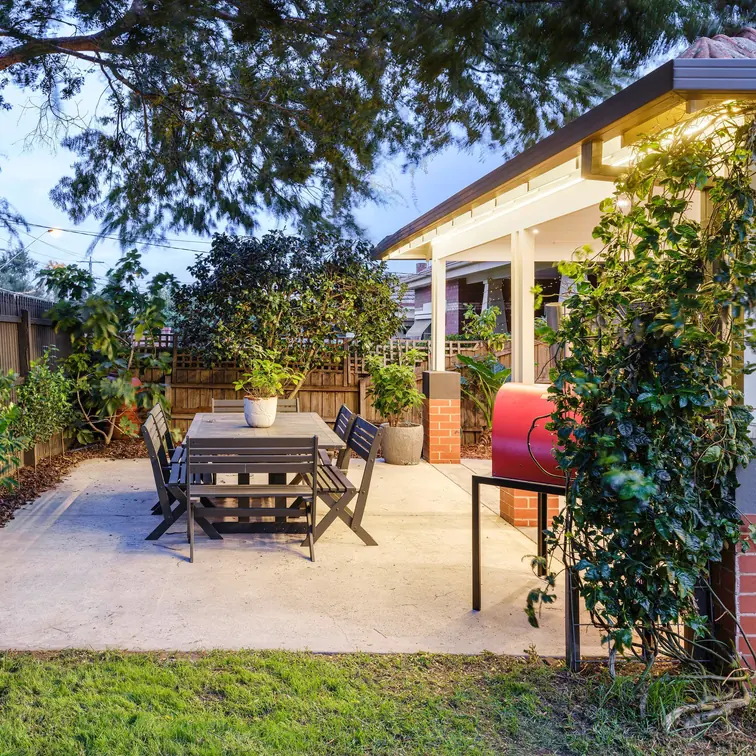 Concrete patio with an outdoor dining setting beside a lit verandah at dusk