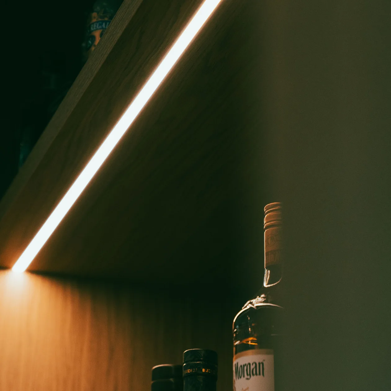 LED strip lighting glowing beneath a timber shelf holding bottles