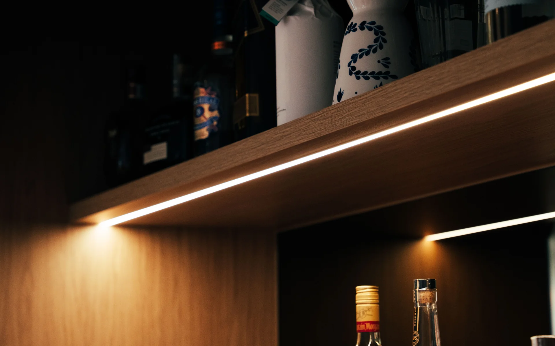 LED strip lighting under timber shelving behind a bar