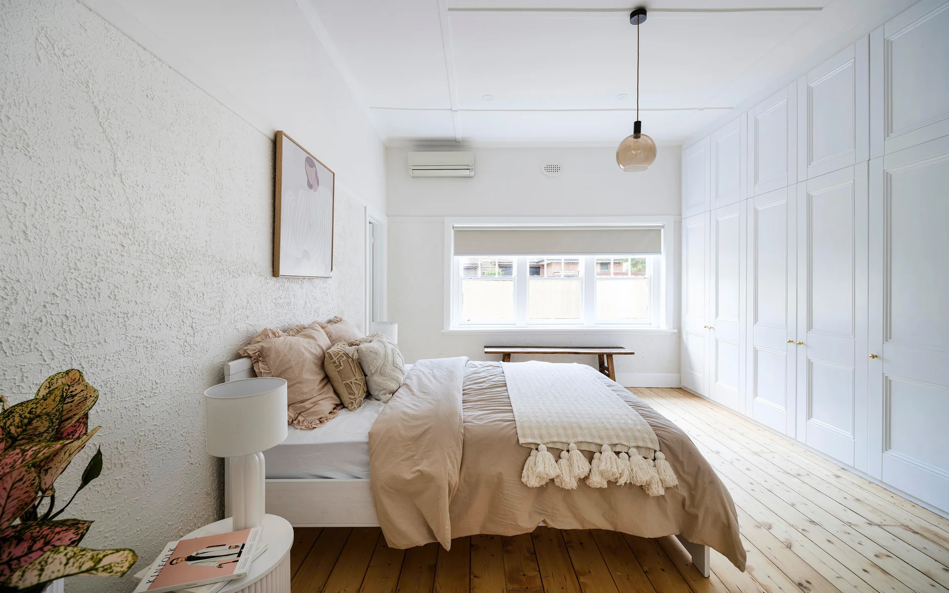 Bright renovated bedroom with timber floors, panelled wardrobes and a woven pendant light