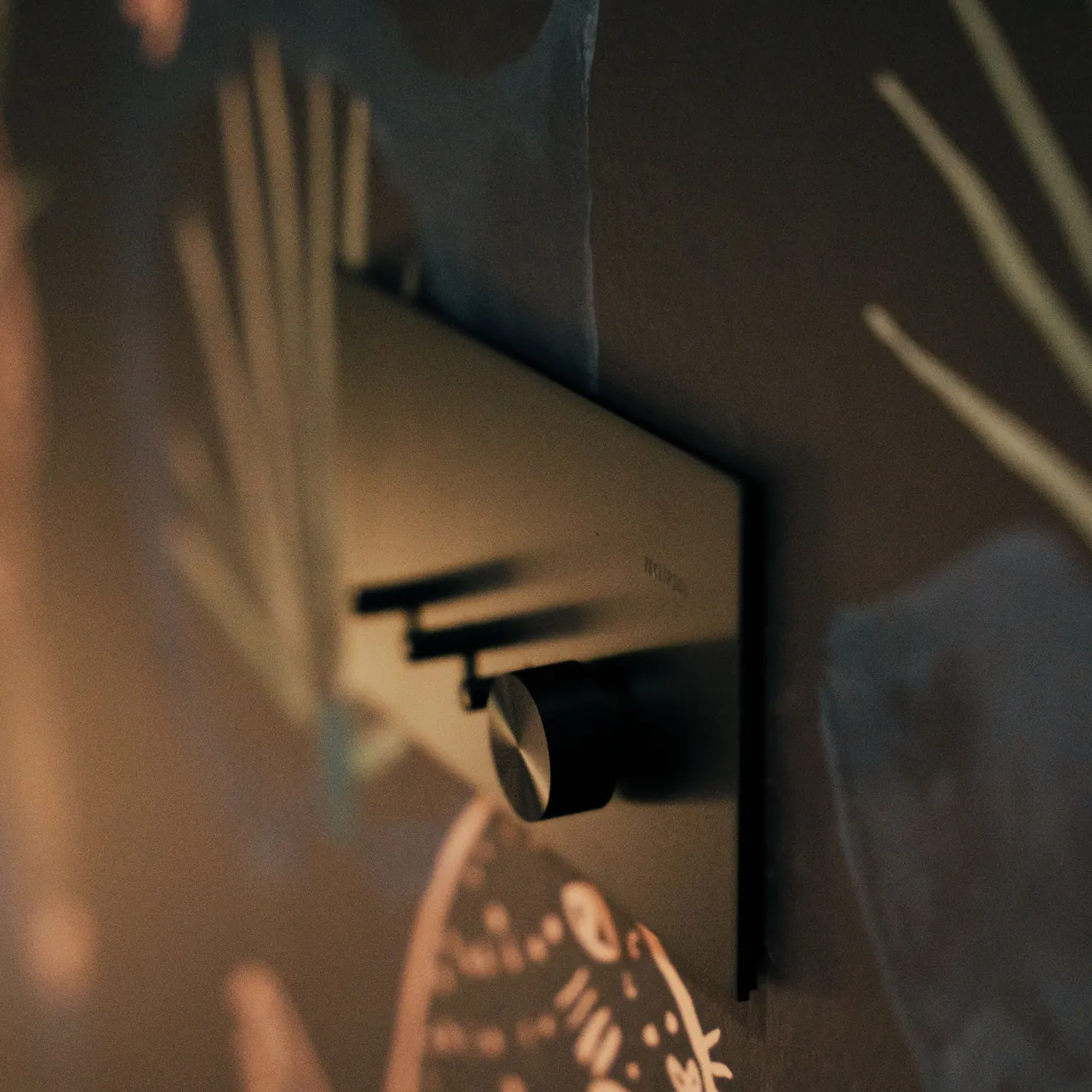 Black wall switch with a metal dial set against dark feature wallpaper