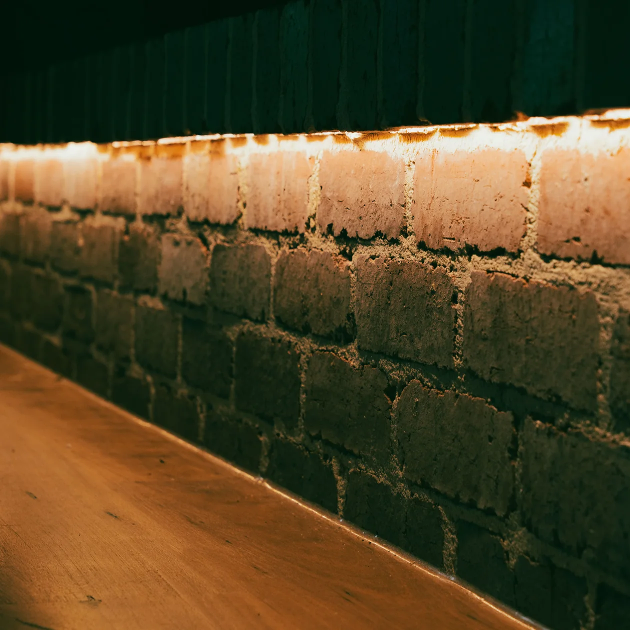 Warm LED strip lighting washing over an exposed brick wall above a timber bench