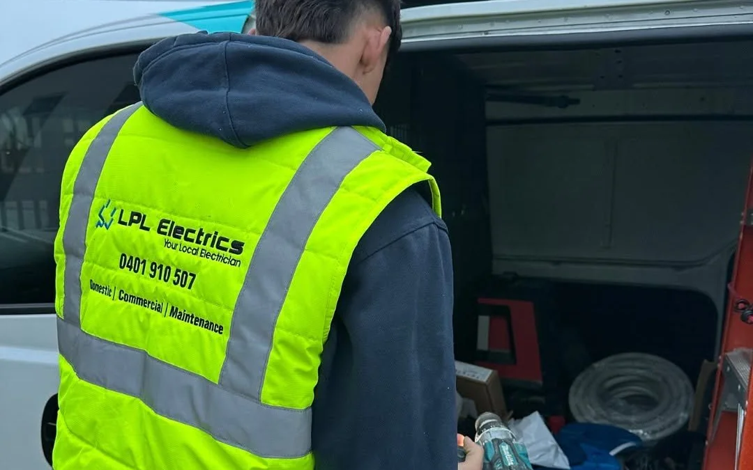 LPL Electrics electrician in a high-visibility vest at the back of a work van
