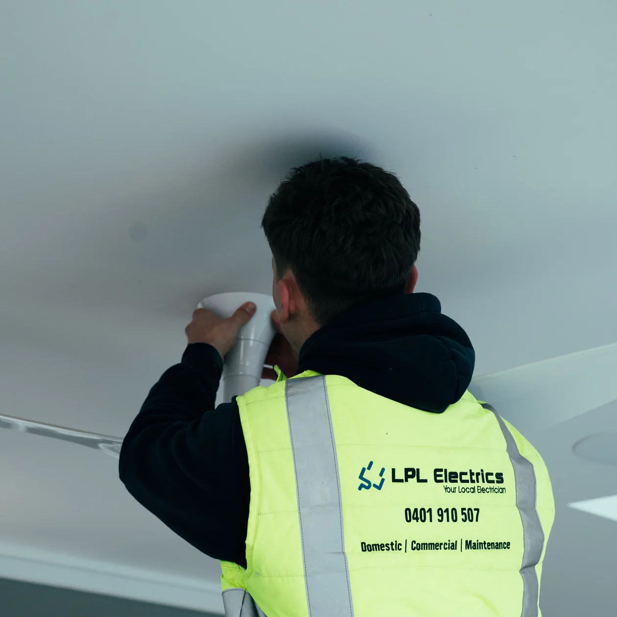 Electrician in a high-visibility vest carrying out electrical work on a ceiling