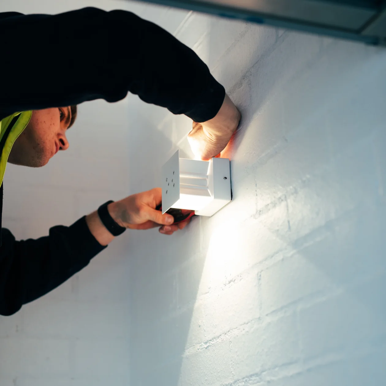 Electrician fitting a white wall light to a painted brick wall