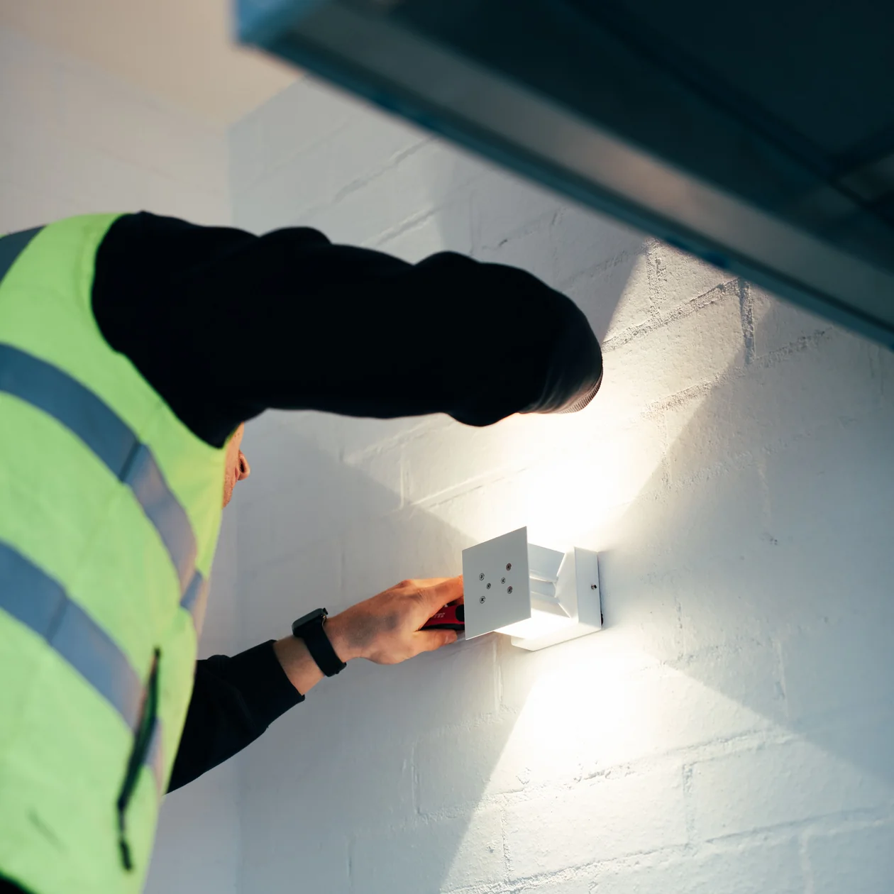 LPL Electrics electrician installing a wall light on a painted brick exterior