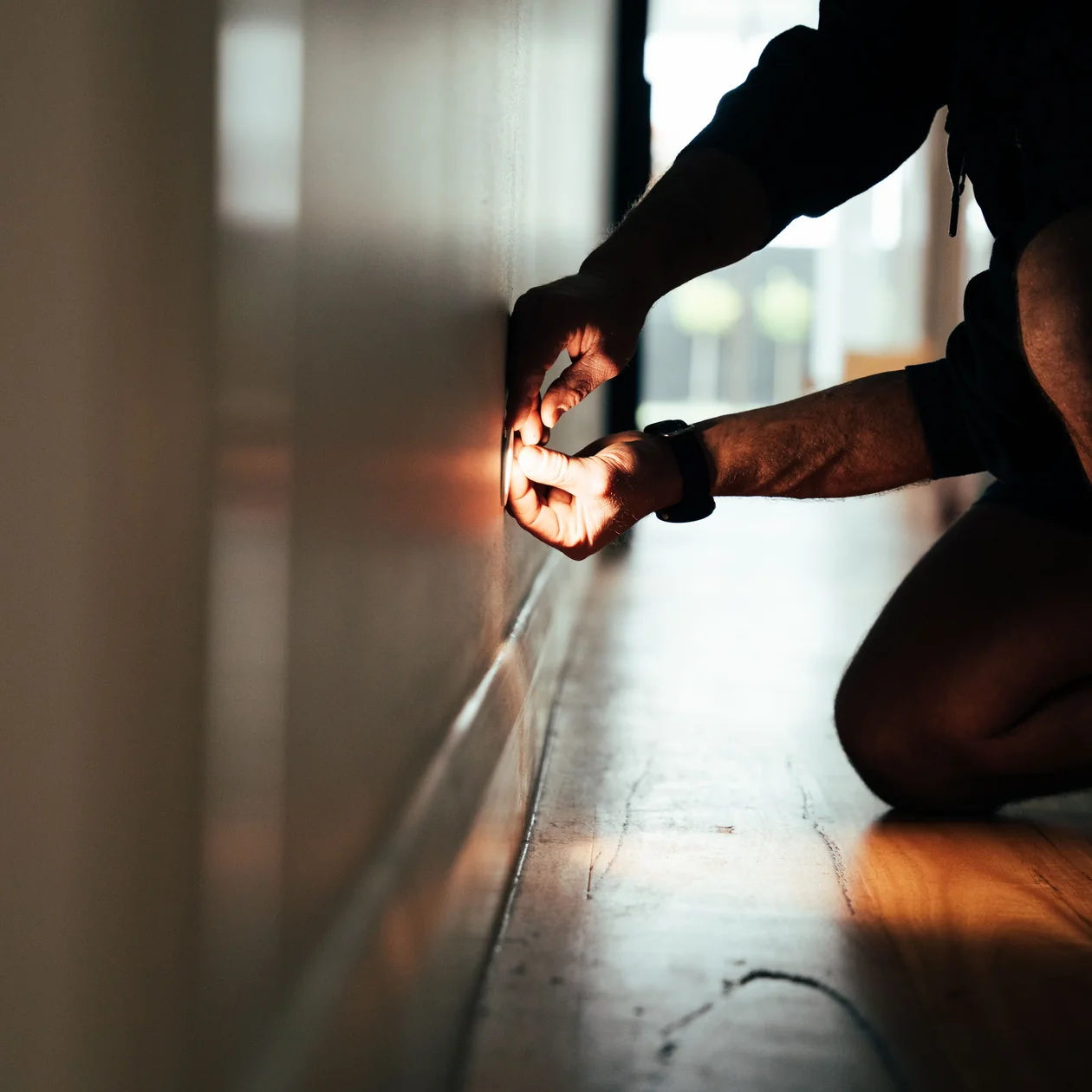 Electrician installing a low-level light beside a timber hallway floor