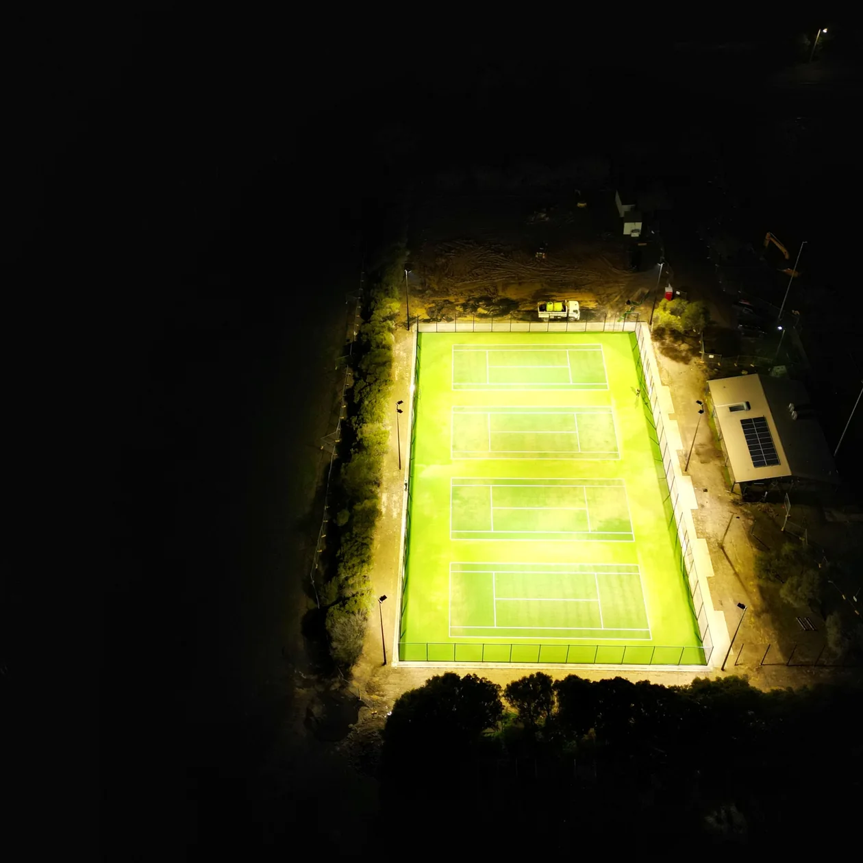 Four tennis courts lit evenly at night, seen from above