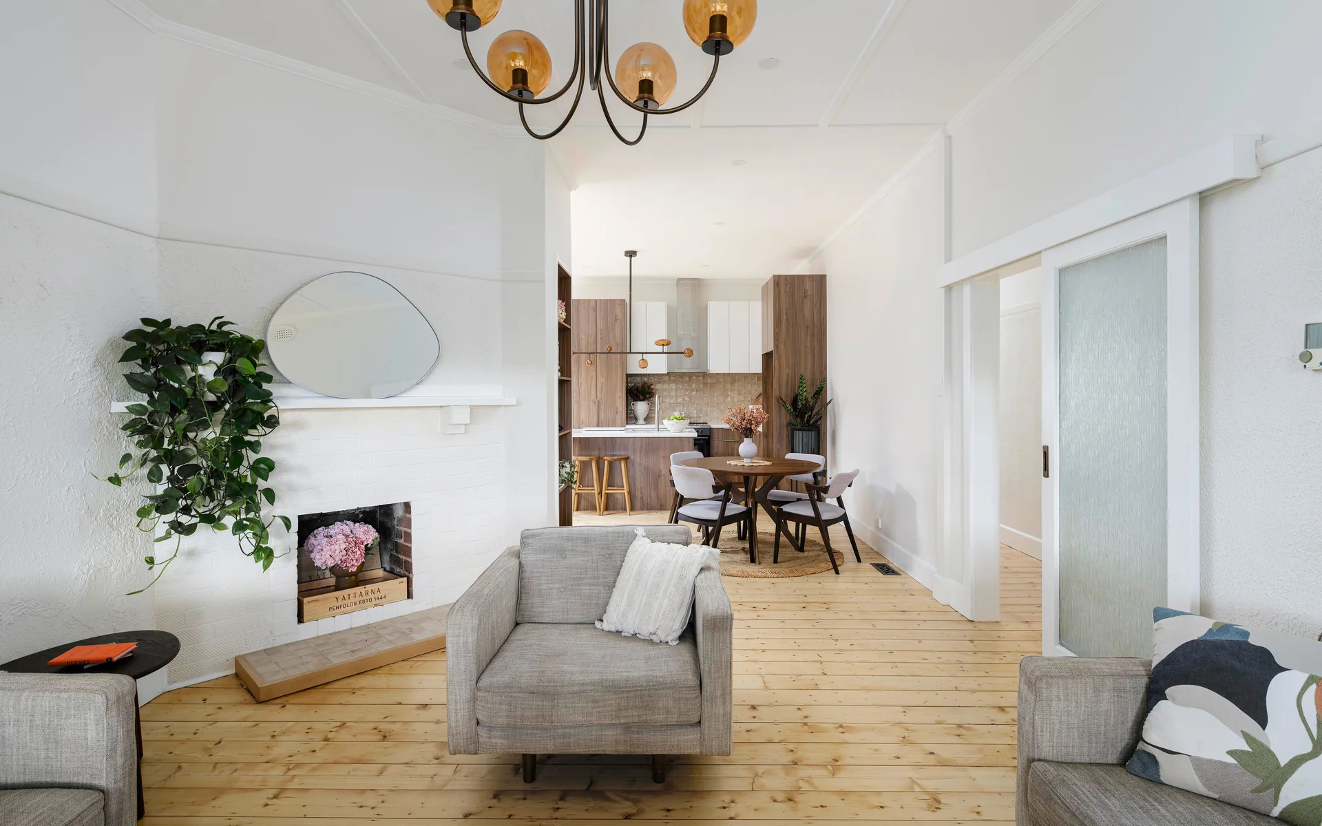 Renovated living room with an amber glass pendant, timber floors and a kitchen beyond