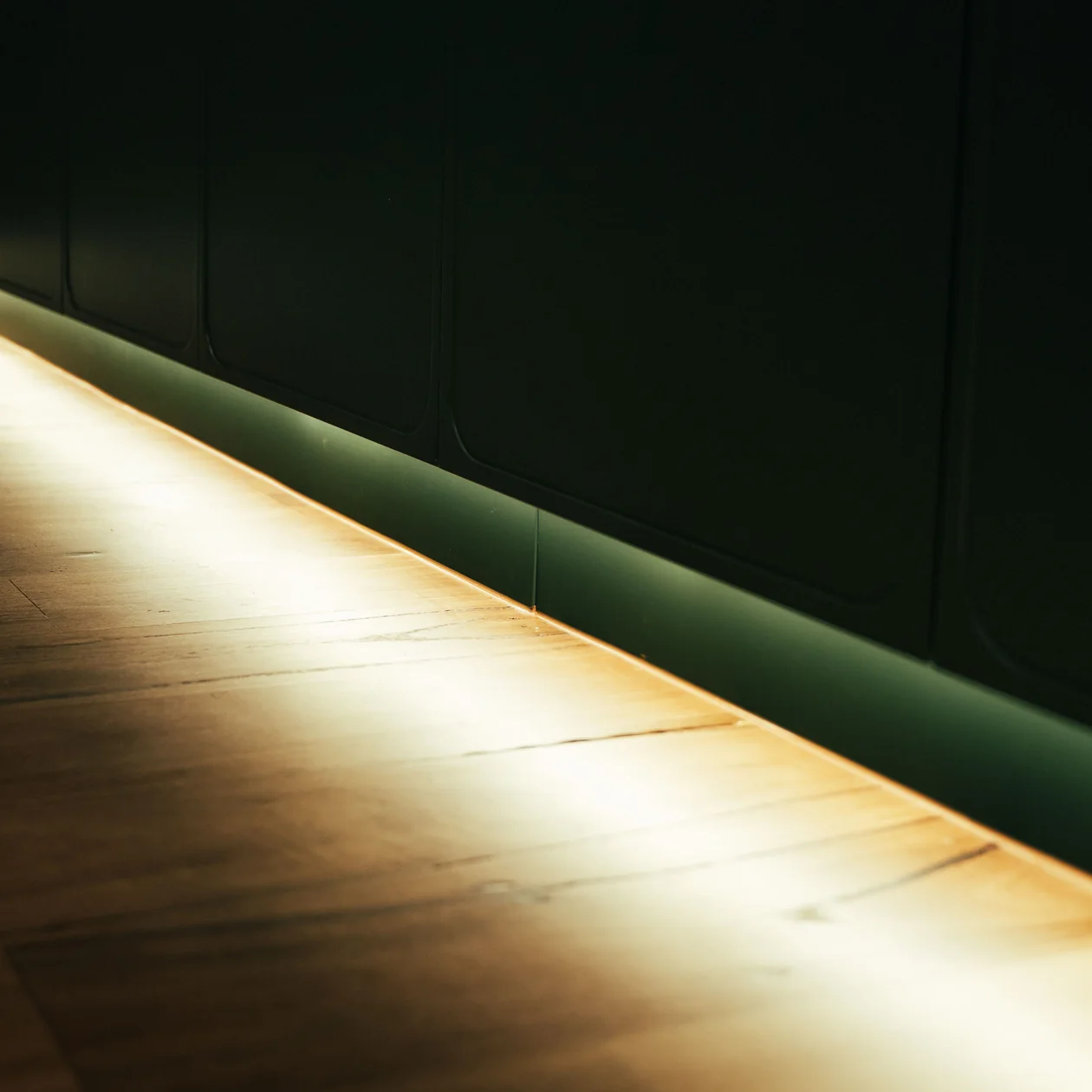 LED strip lighting glowing along the base of dark green joinery