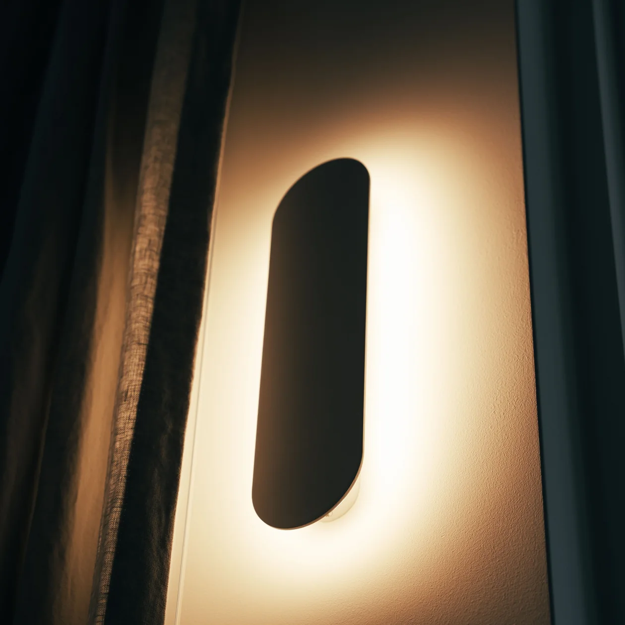 Oval wall light casting a warm glow on a wall beside a curtain