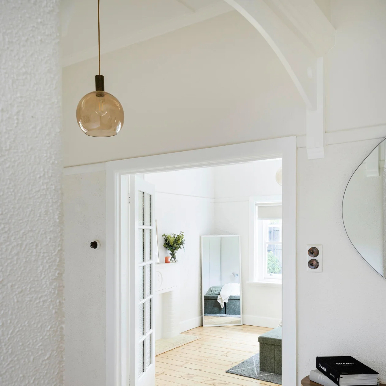 Amber glass pendant hanging in a white hallway beside a doorway into a bedroom