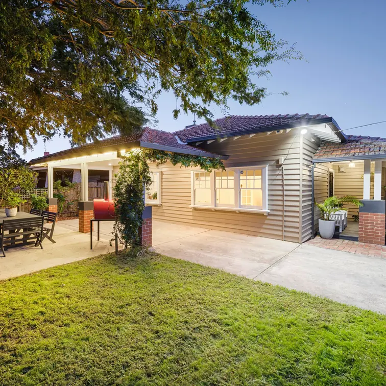Weatherboard home with a paved yard and exterior lights glowing at dusk