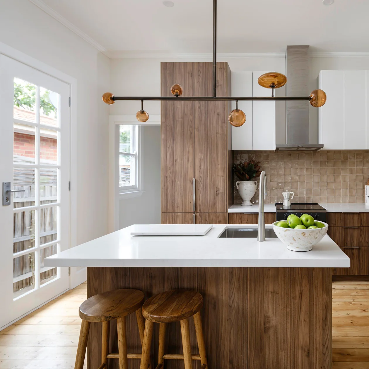 Renovated kitchen with timber joinery, a white island bench and a bar pendant with amber glass globes