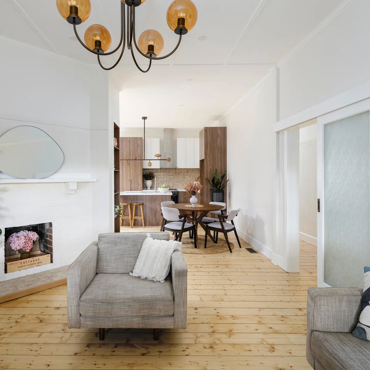 Bright living room with grey armchairs and a globe chandelier looking through to a dining table