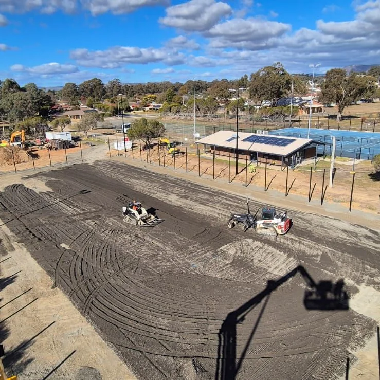 Machinery grading the base of a sports court during construction
