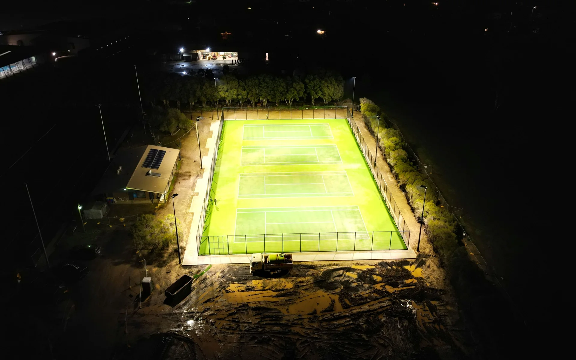 Aerial view of four outdoor tennis courts lit by pole-mounted lights at night