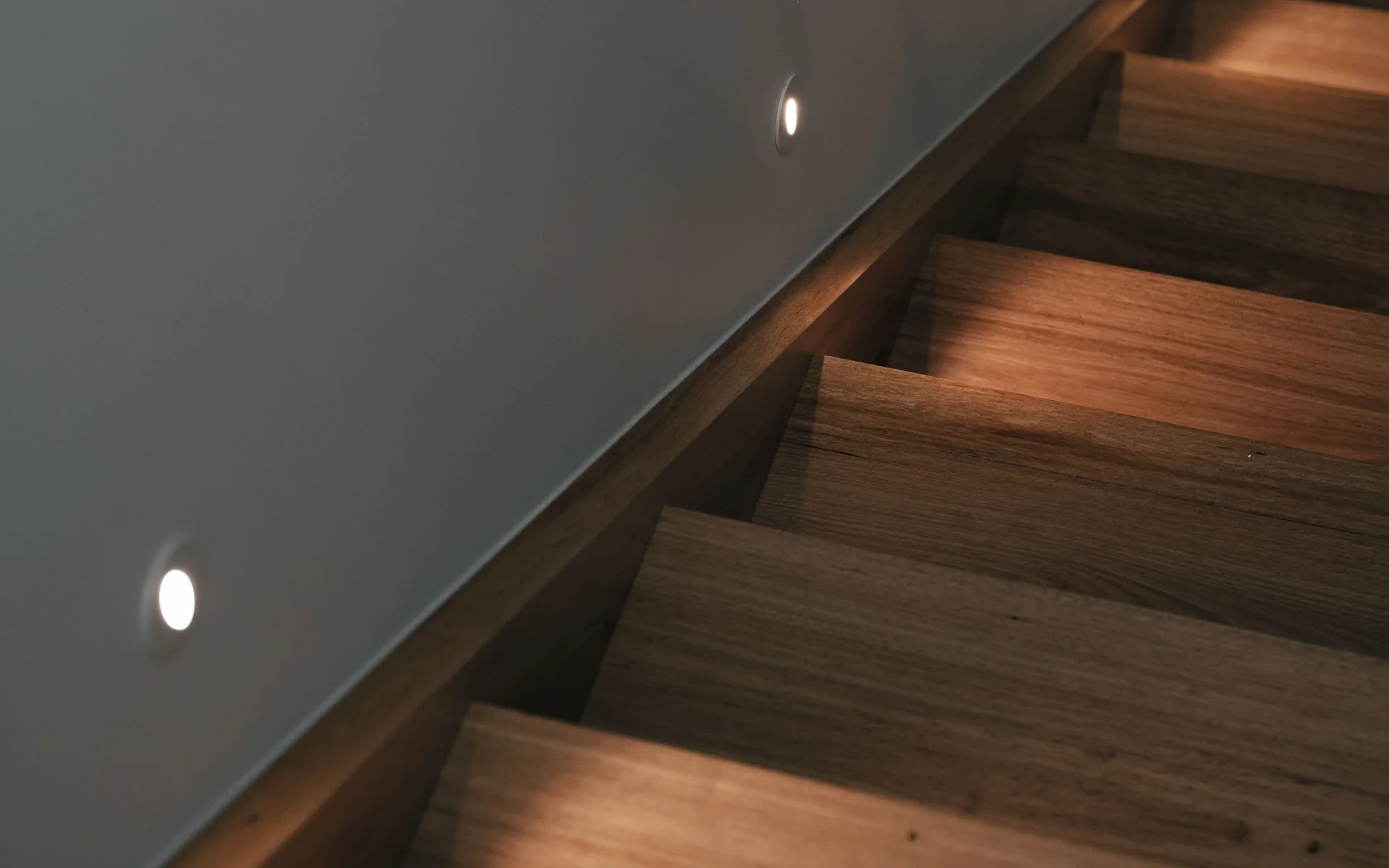 Round LED step lights set into a grey wall beside timber stairs