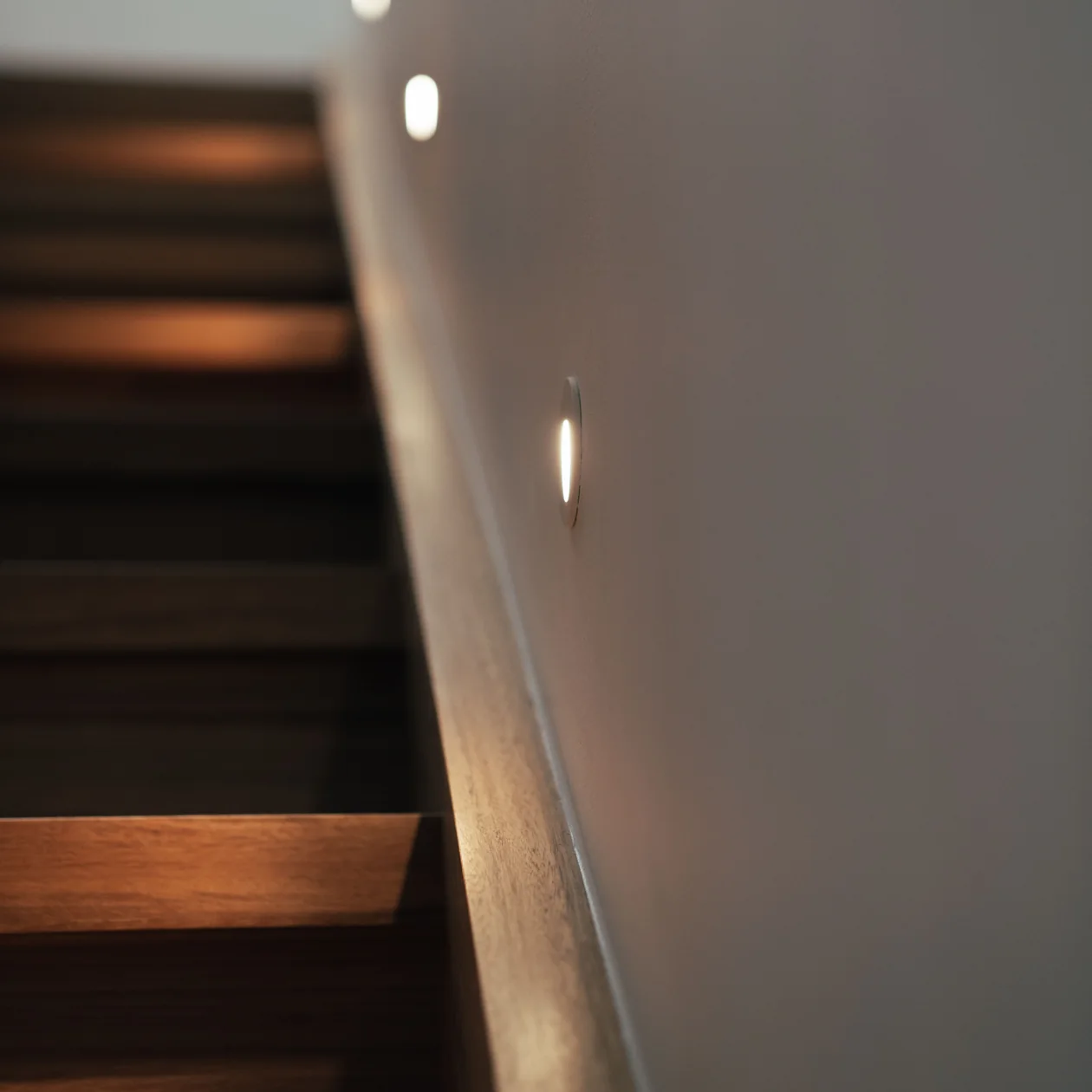 Round step lights set into a wall beside a timber staircase