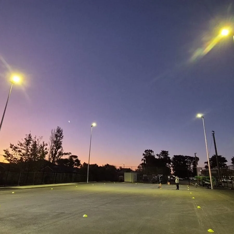 Tall light poles switched on around an outdoor court at dusk