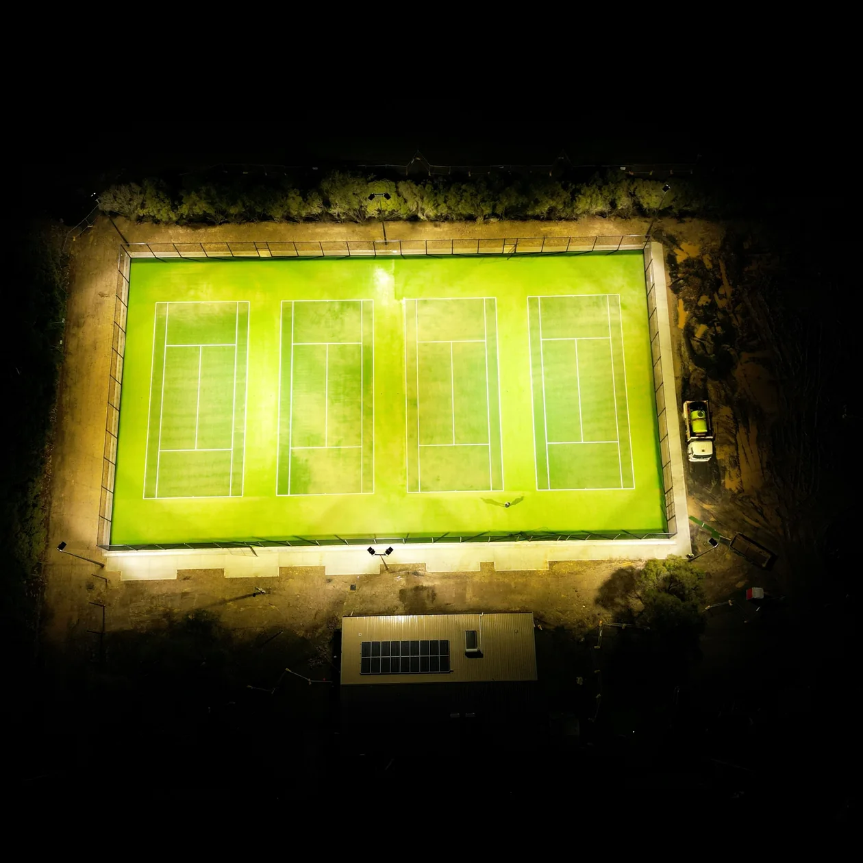 Overhead view of four floodlit tennis courts at night
