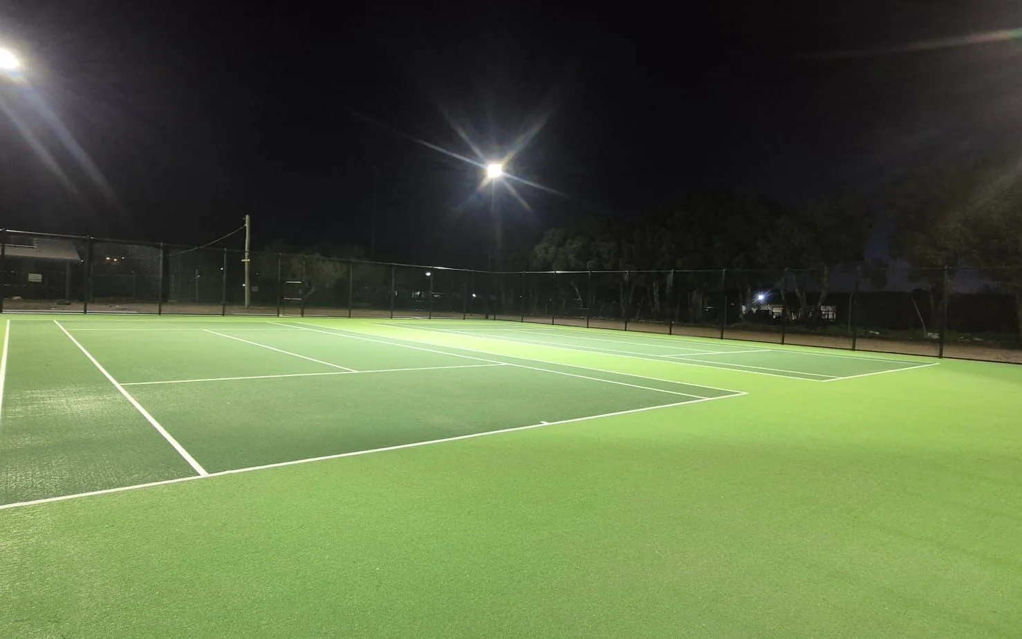 Floodlights on tall poles lighting synthetic tennis courts at night