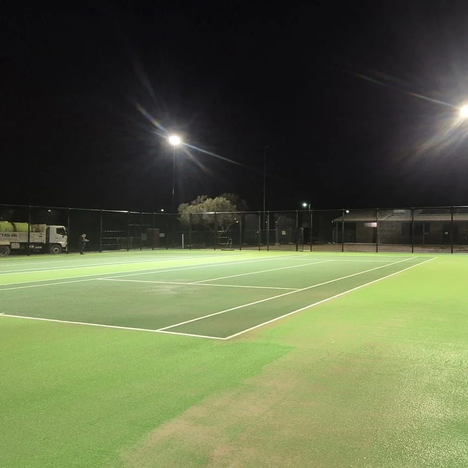 Floodlights shining over a green synthetic tennis court at night