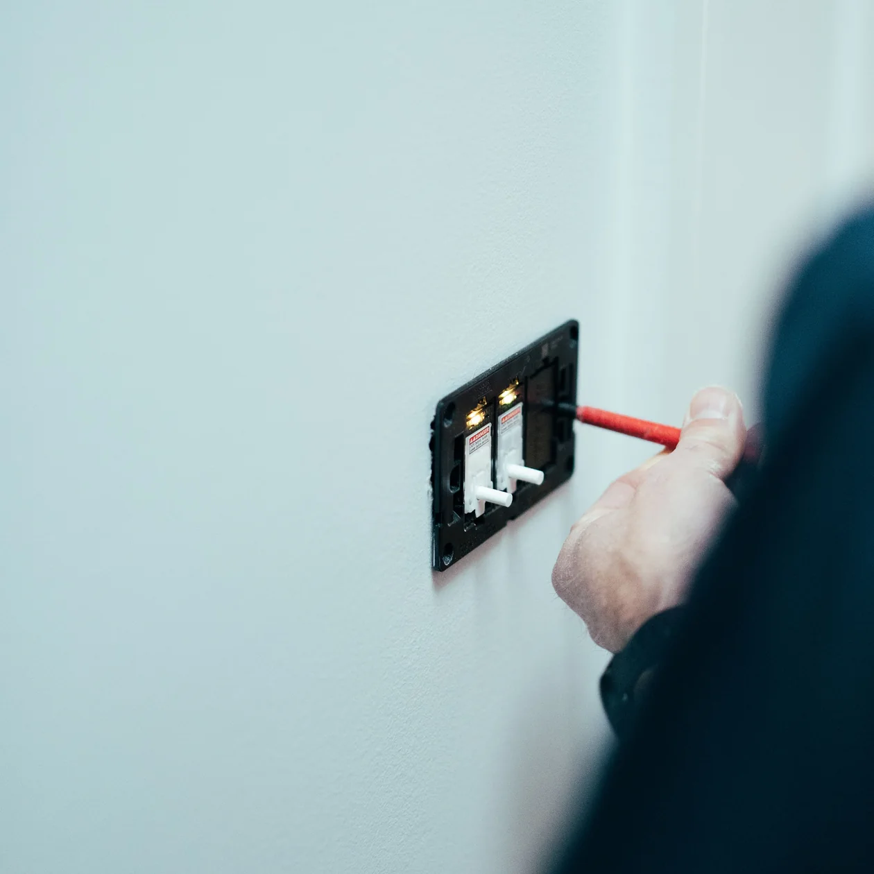 Electrician working on an open wall switch mechanism with a red-handled screwdriver