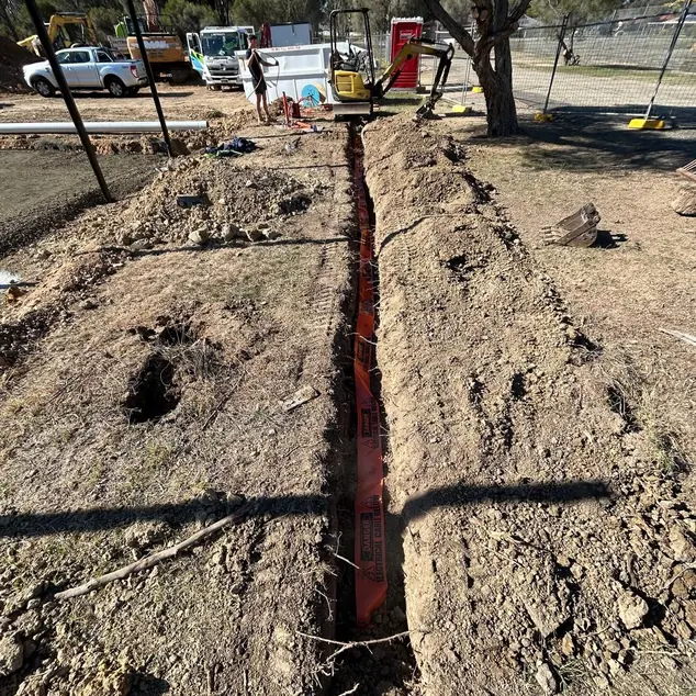 Orange electrical conduit being laid in an open trench on a work site