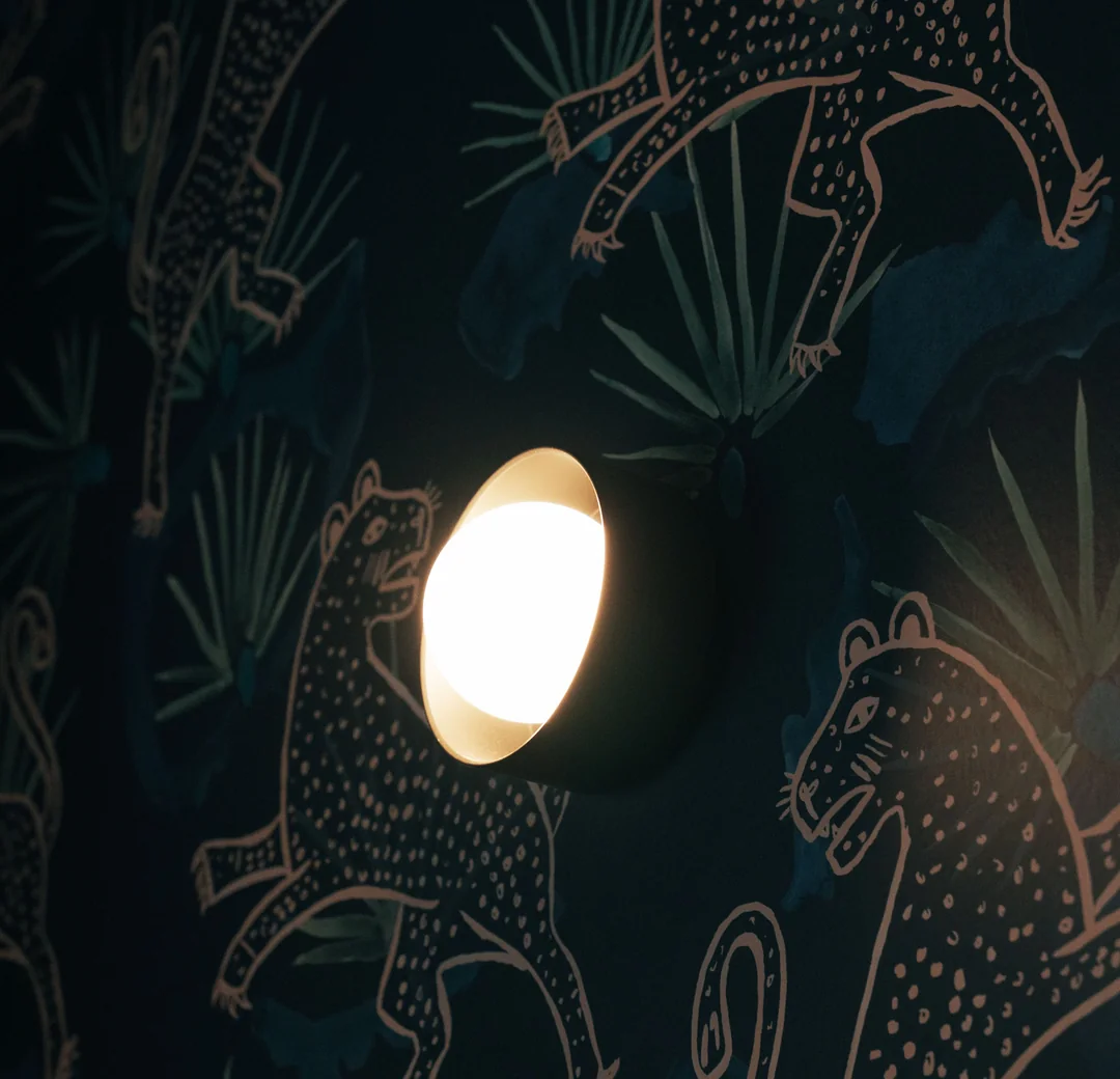 Round wall light glowing against dark patterned wallpaper