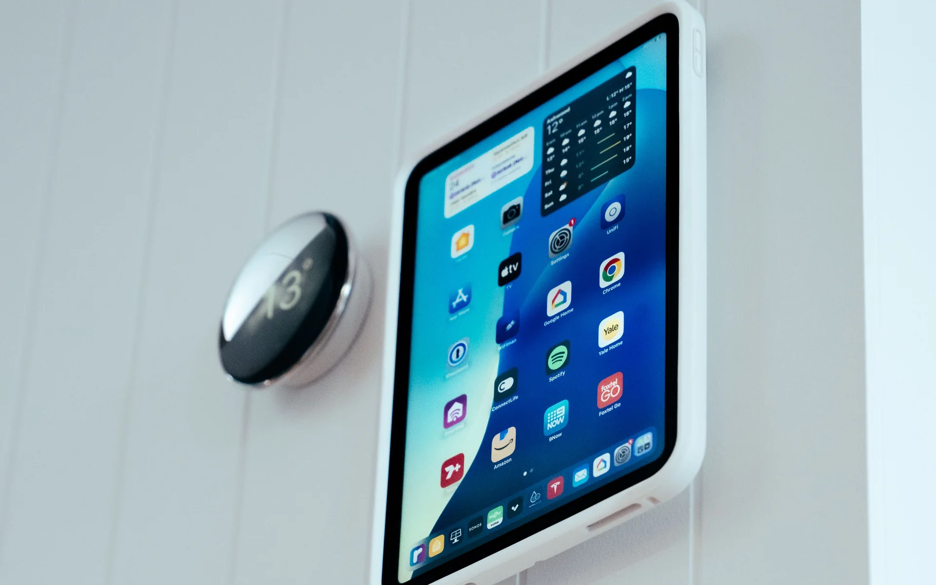 Wall-mounted iPad beside a round thermostat on a white panelled wall