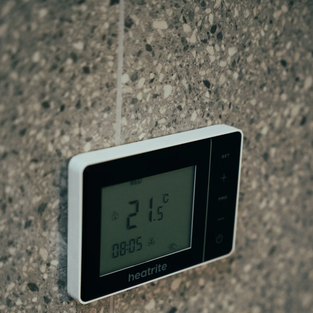Digital thermostat mounted on a speckled tiled wall